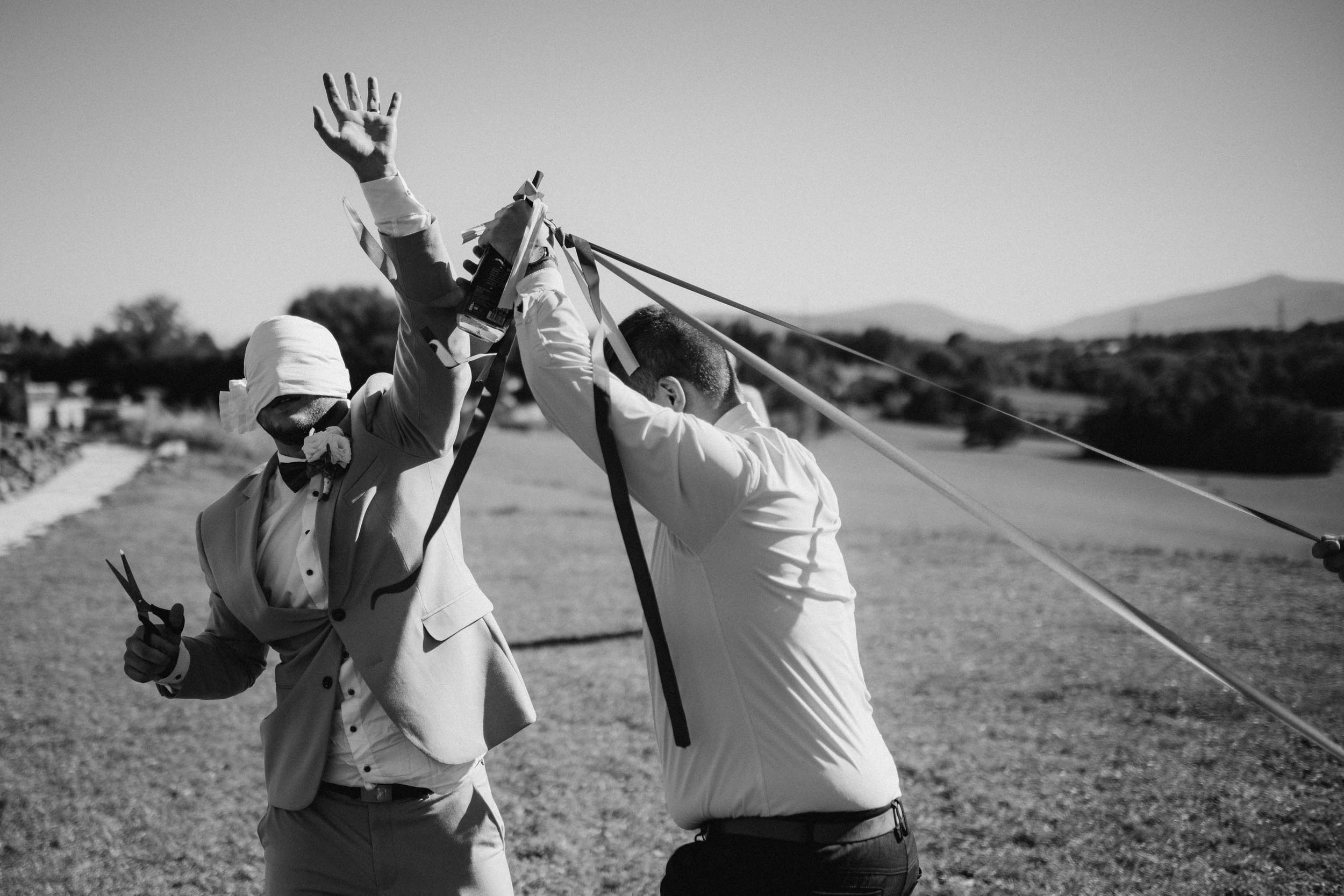 Black and white photo of wedding guests posing with raised arms against a countryside backdrop.