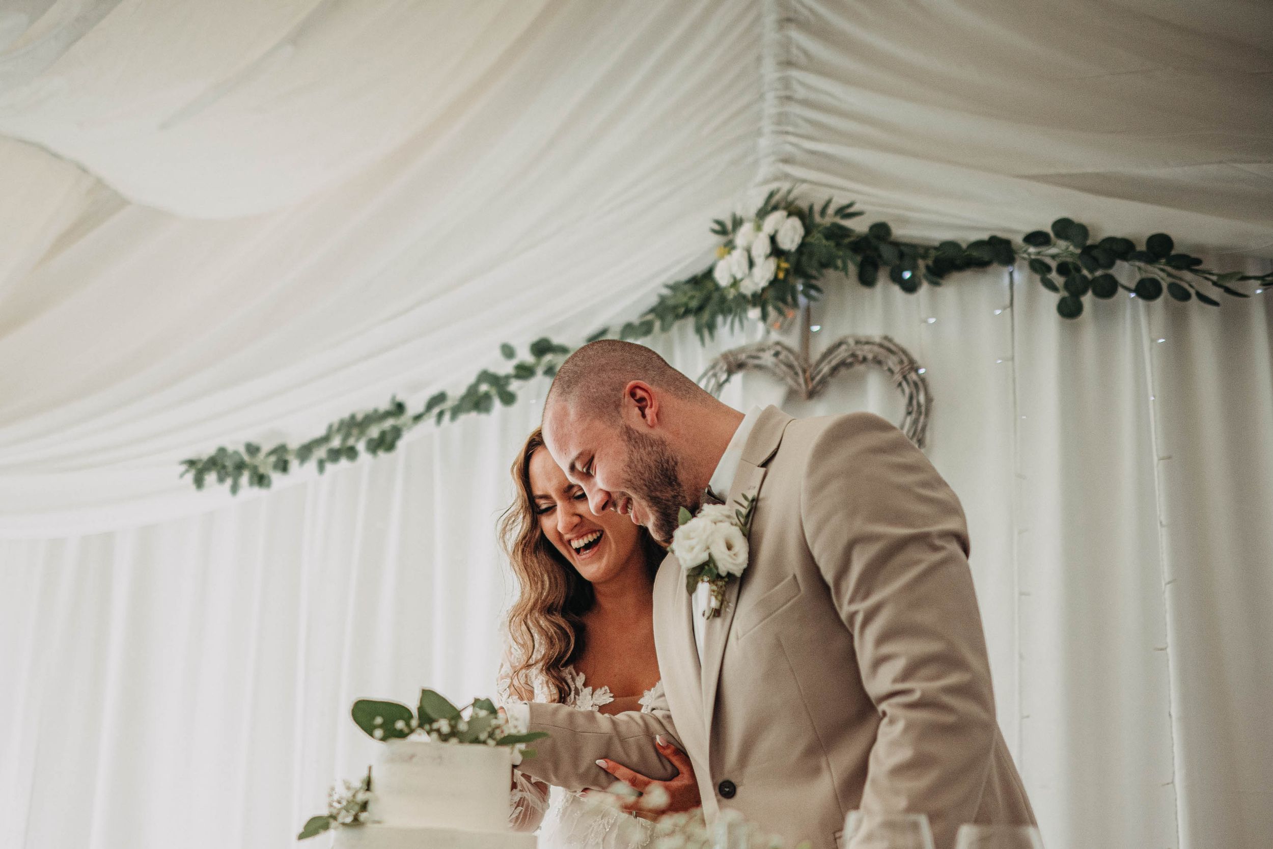 Wedding party celebrates with champagne toasts under a white tent decorated with greenery.
