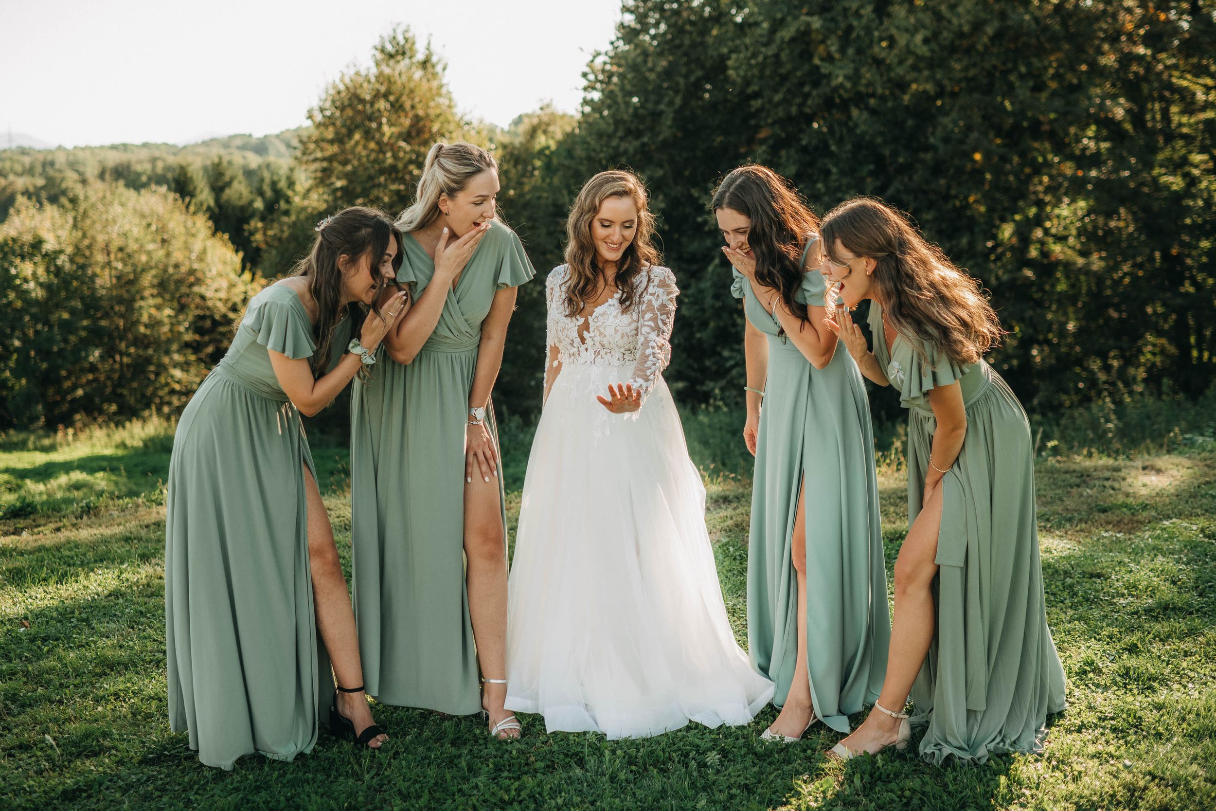 Wedding party in sage green dresses posing together on a scenic hilltop at sunset.