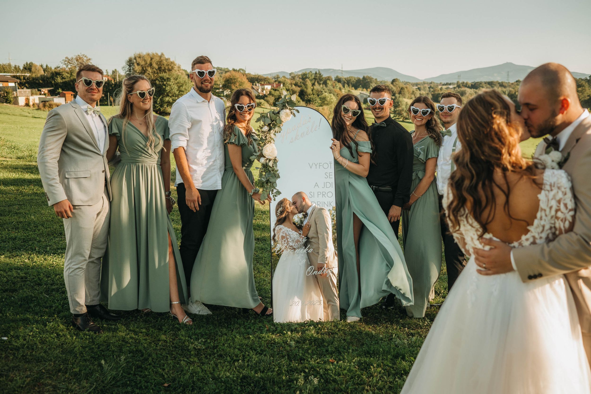 Wedding party gathered outdoors for group photos in a scenic mountain setting.