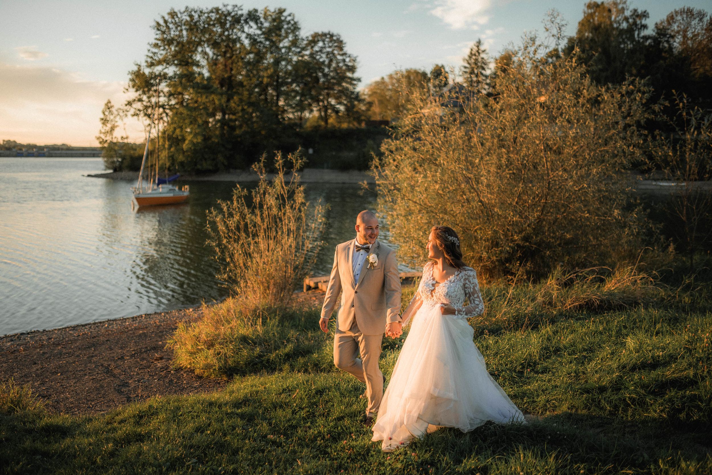 Sunset wedding portraits captured along a scenic waterfront with fall foliage.