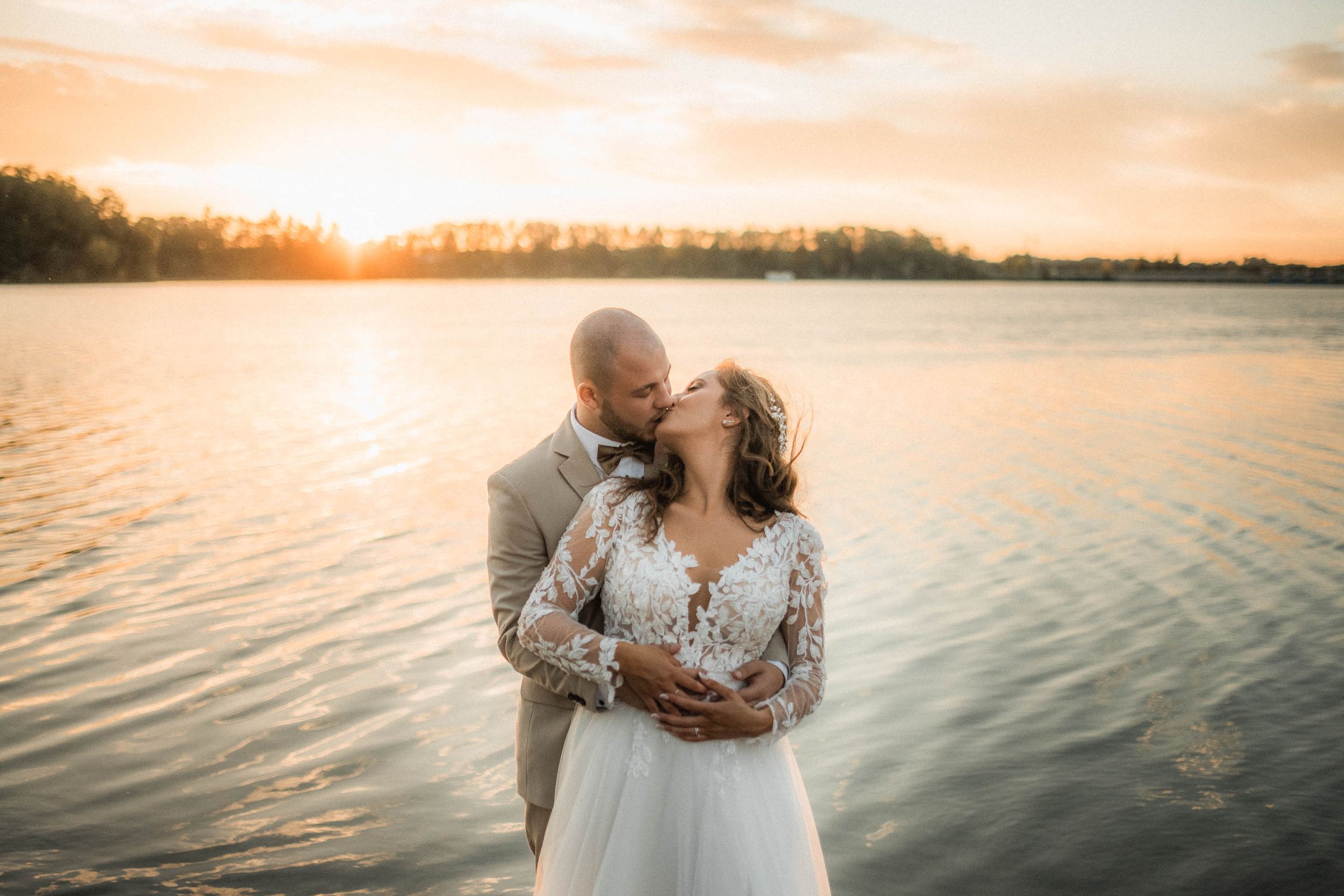 Dreamy waterfront wedding portraits during a vibrant orange sunset.