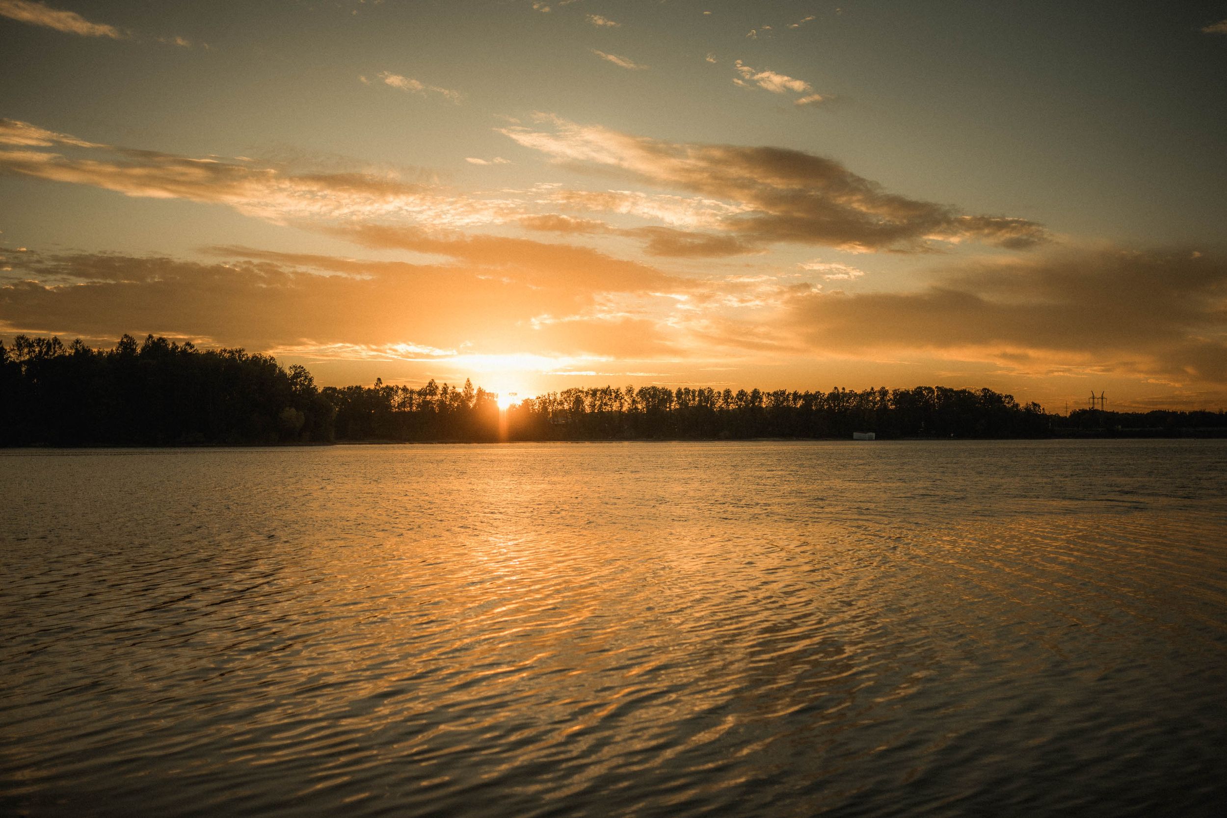 Panoramic sunset landscape over a lake with silhouetted treeline and orange sky.