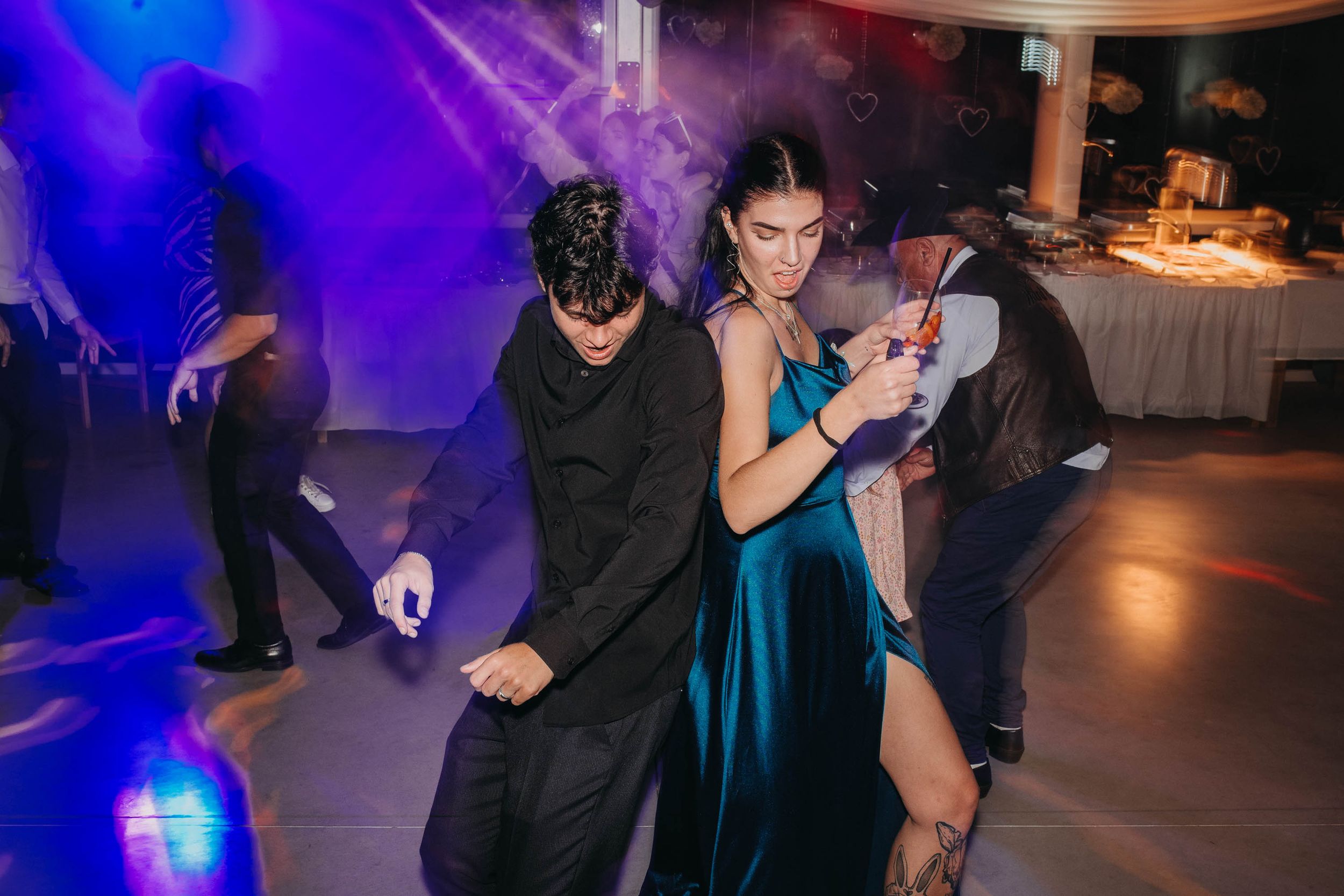 Wedding guests dancing energetically at a reception with purple lighting and festive atmosphere.