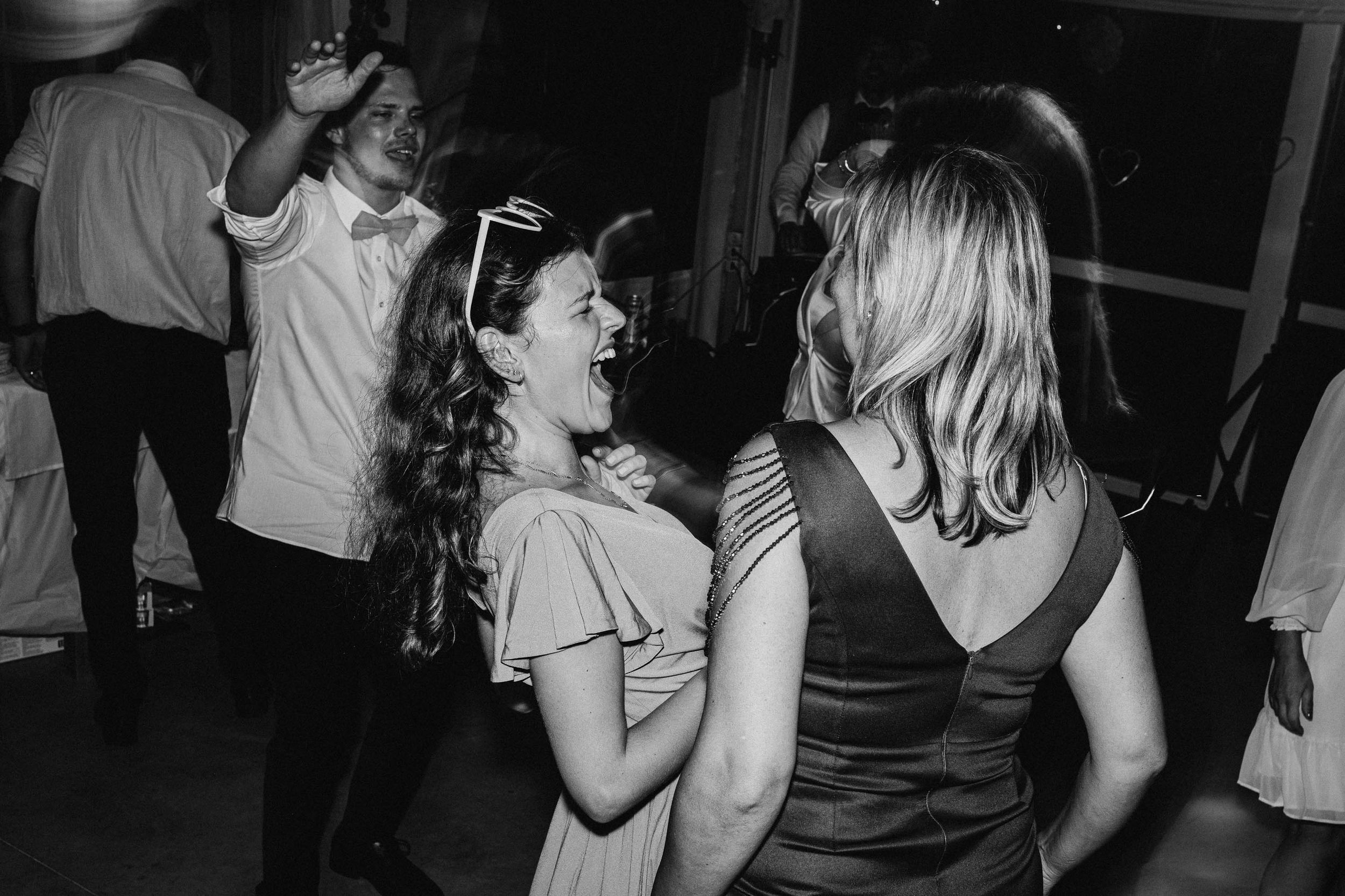 Wedding guests enjoying themselves on a dimly lit dance floor at an evening reception.