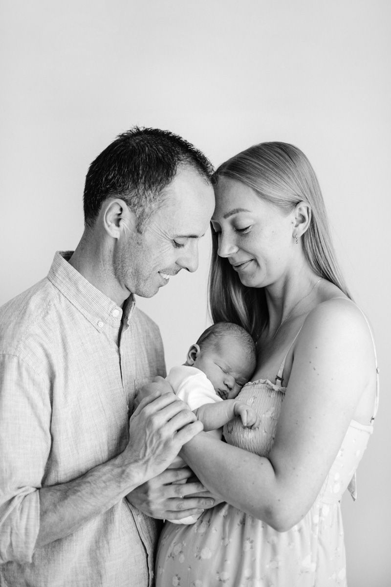 A series of four black and white photos showing tender moments between parents and their newborn baby.
