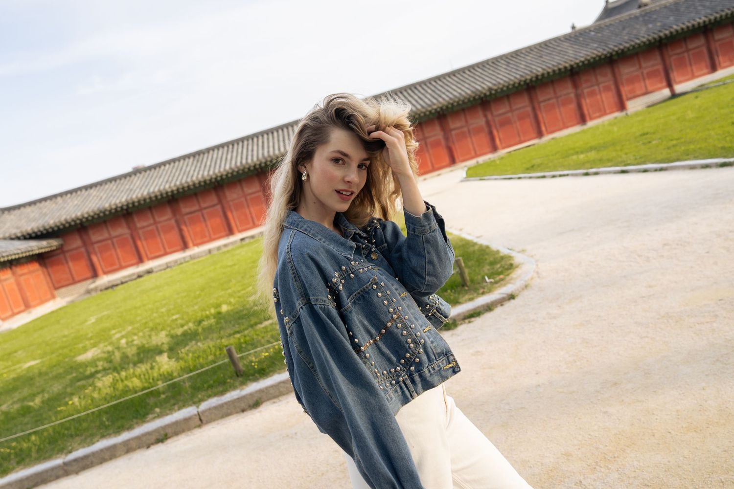Person in denim jacket walking through outdoor location with red brick wall and grass in background.
