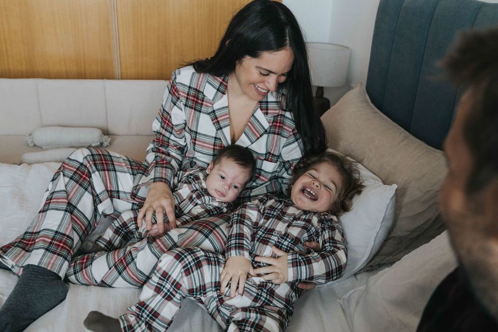 A parent and child in matching plaid pajamas share playful moments together on a gray couch.