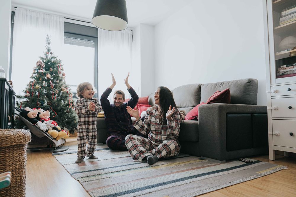 Family in matching plaid pajamas celebrating together in cozy living room with decorated Christmas tree.