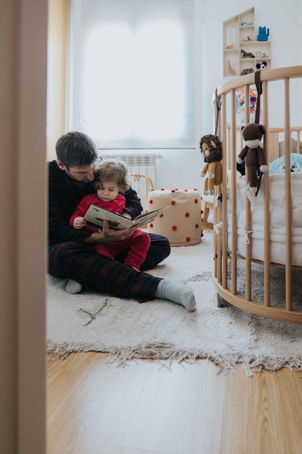 A cozy reading moment in a nursery with stuffed animals on a round crib and a plush rug on wooden floors.
