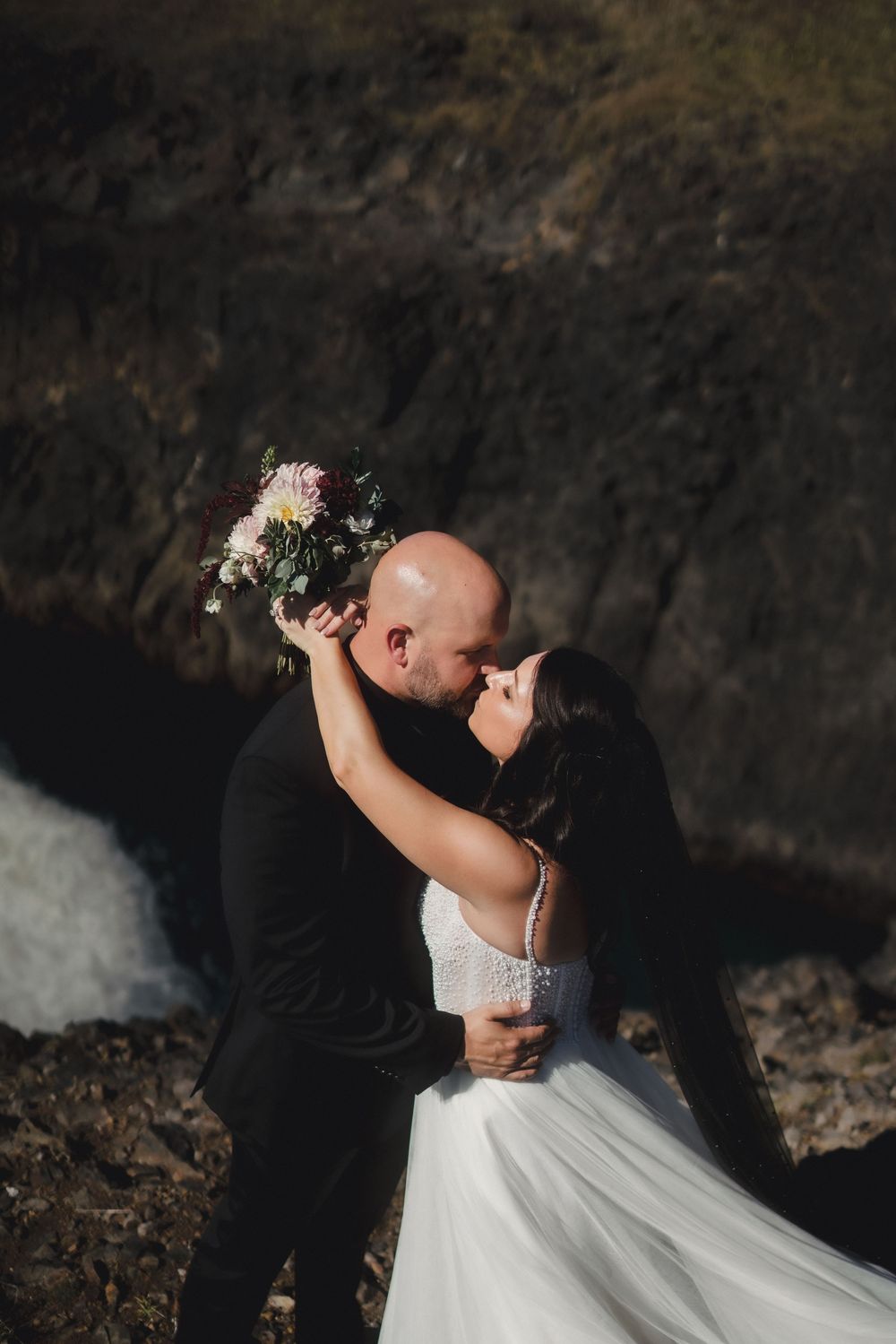 A romantic wedding couple shares intimate moments in a dramatic dark setting with the bride wearing a flowing white dress.