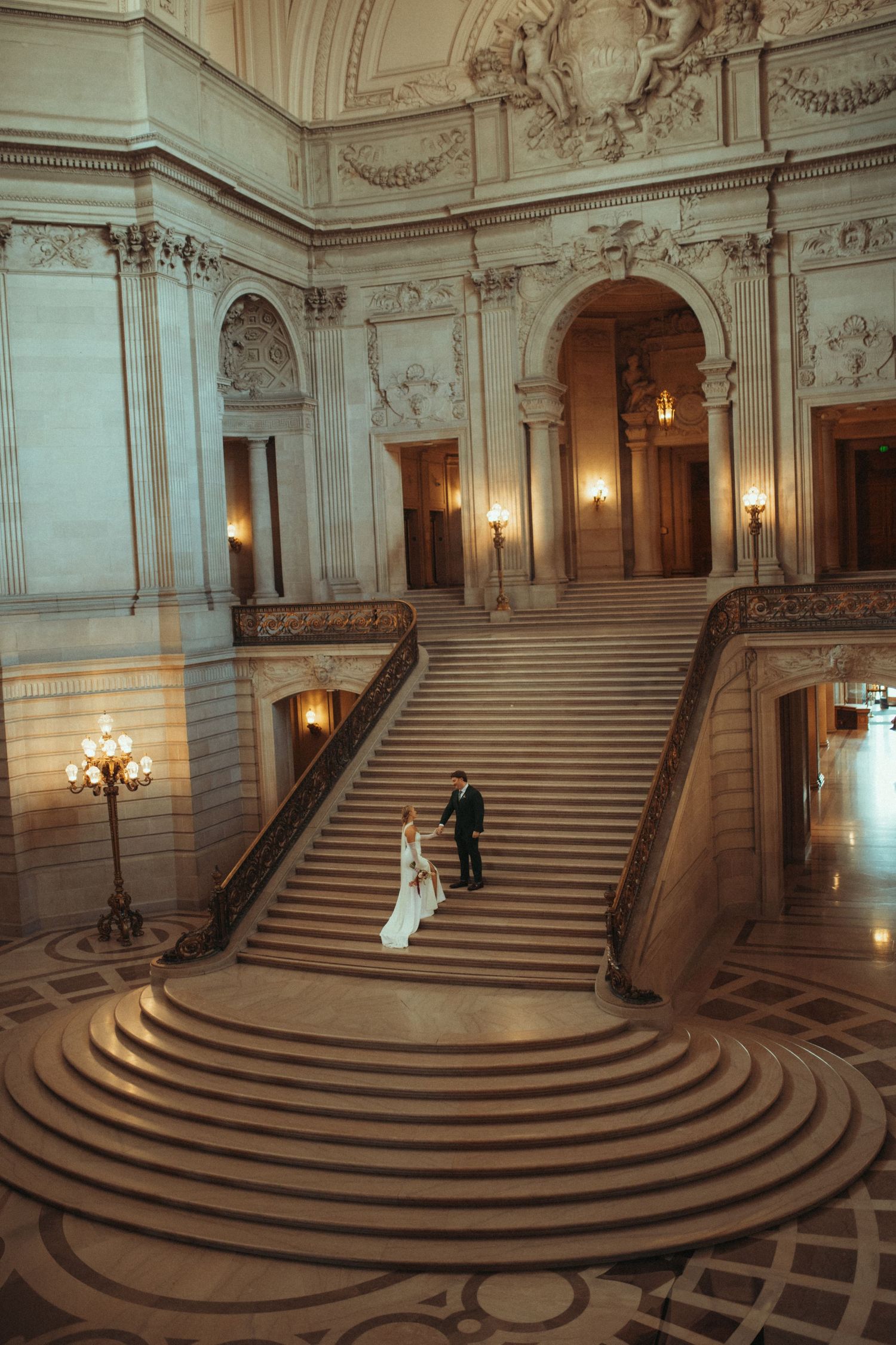 A panoramic view of an ornate marble staircase in San Francisco City Hall with elegant architectural details and wall sconces.