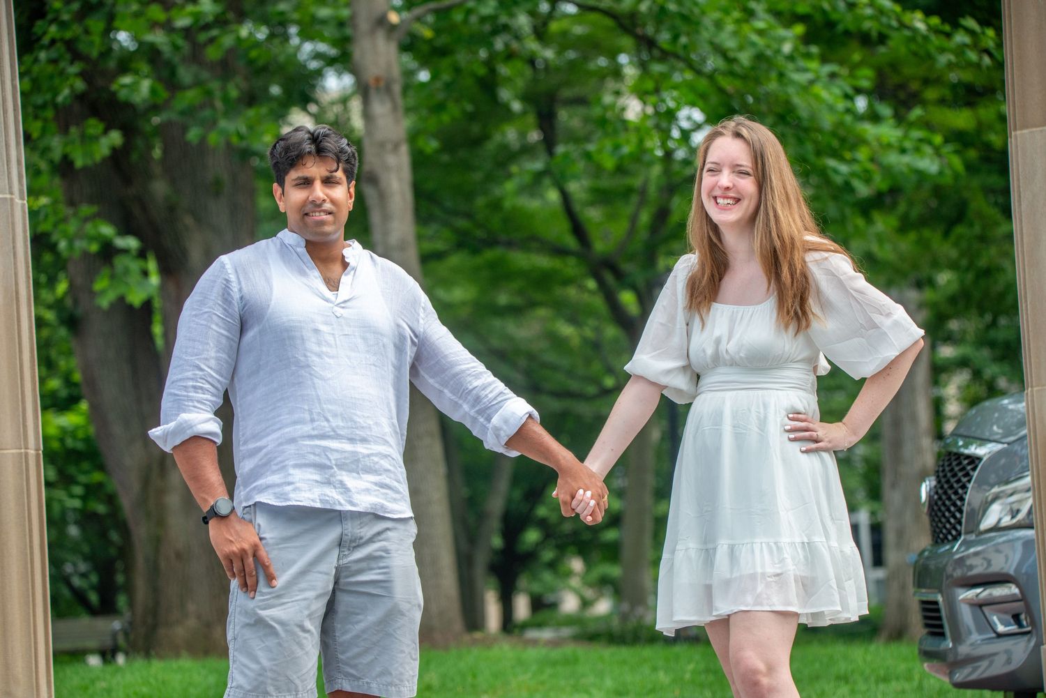 A group in light colored clothing holds hands while walking together through a lush green park setting.