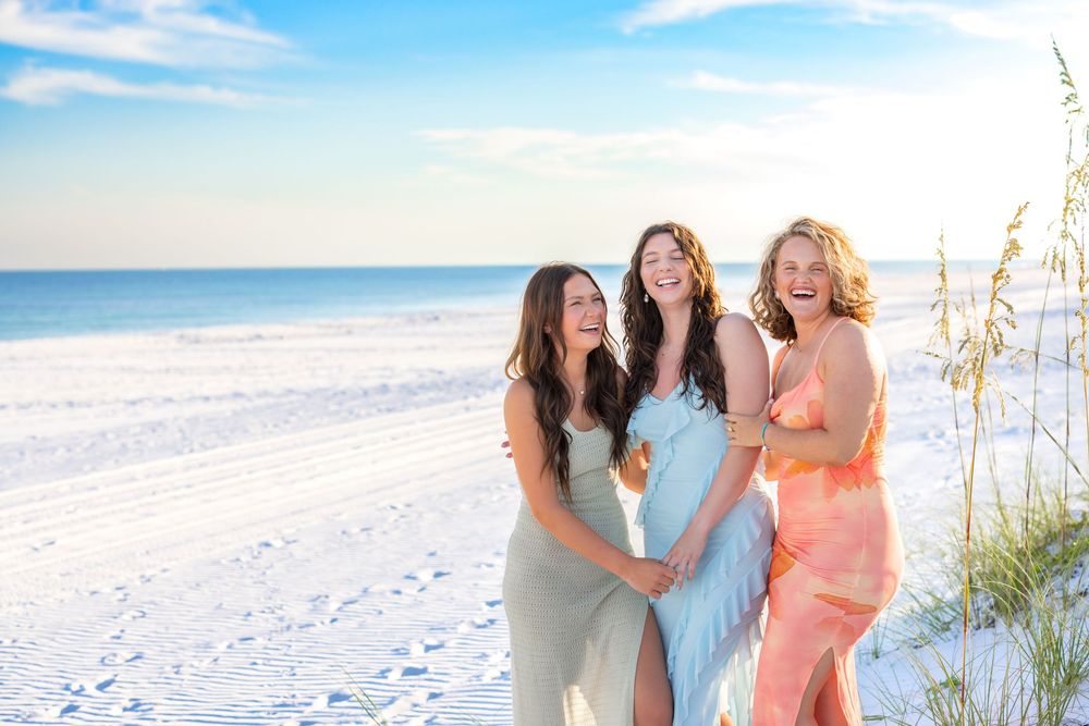A group of people enjoying a sunny day together at a white sandy beach with sea oats in the background.
