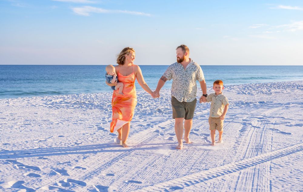 People walking along a pristine white sandy beach with clear blue ocean waters and tire tracks in the sand.