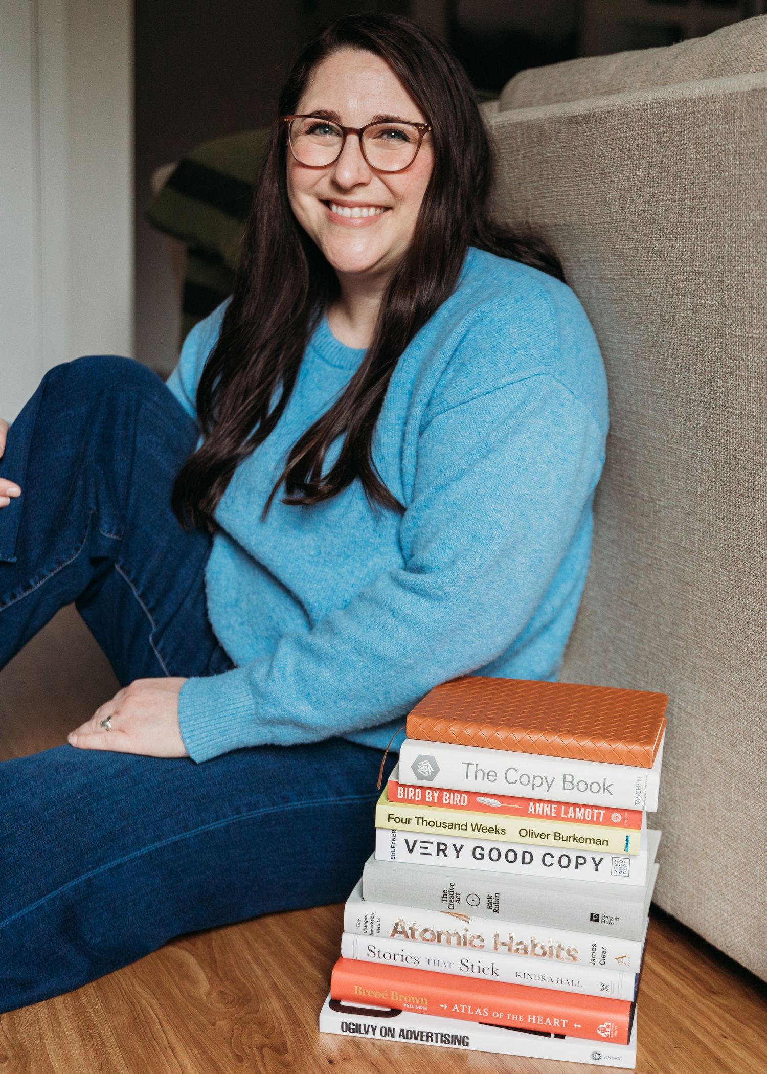 Someone wearing a light blue sweater sits on a couch while reading a self-help book about atomic habits.