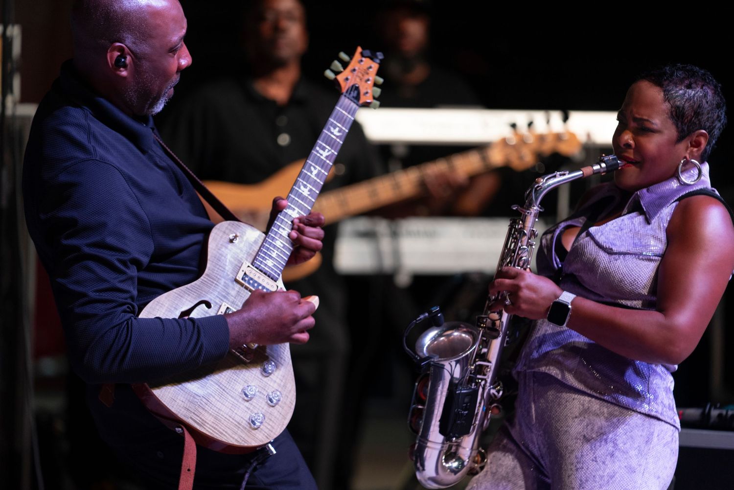 Musicians perform on stage with guitars during a live blues or jazz concert in a dimly lit venue.