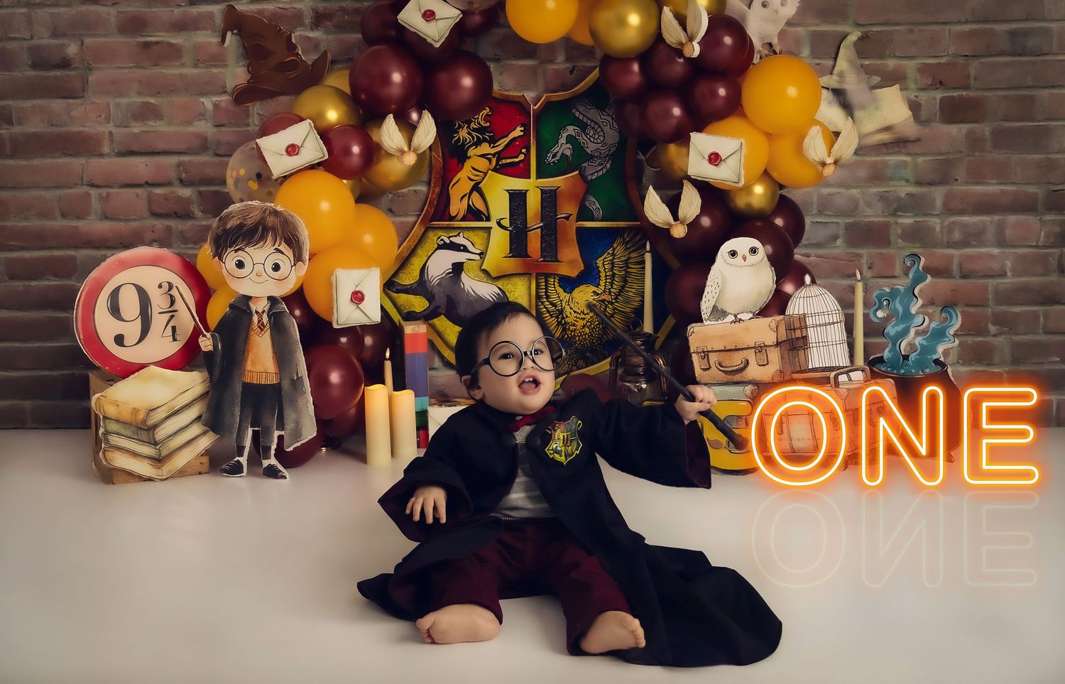 A Harry Potter themed birthday setup with magical decorations, wands, books, and illuminated ONE sign against a brick wall.