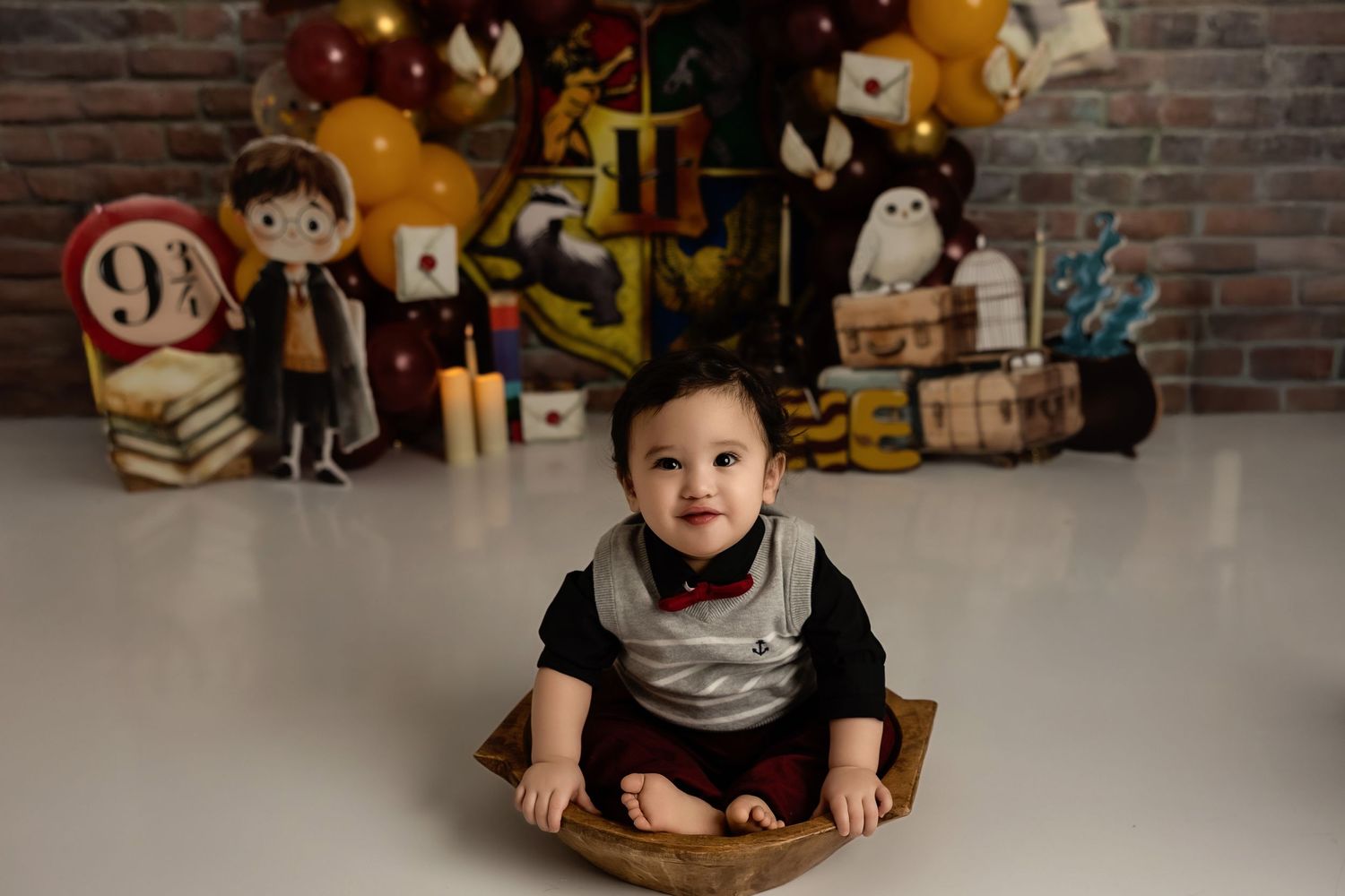 A baby sits in front of a themed party display with Harry Potter decorations against a brick wall background.