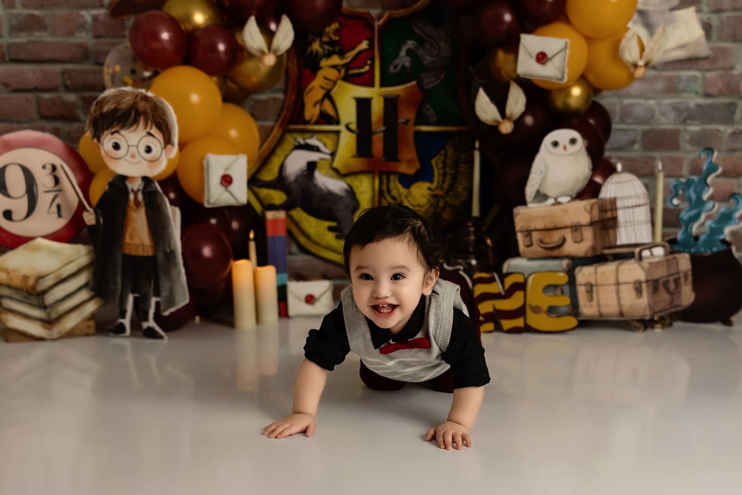 Harry Potter themed cake smash setup with magic decorations, balloons, and props against a brick wall backdrop.