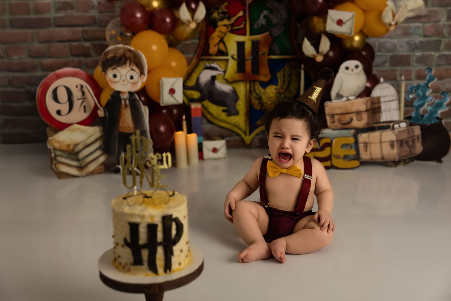 A Harry Potter themed first birthday celebration with a black and gold cake and magical decorations in the background.