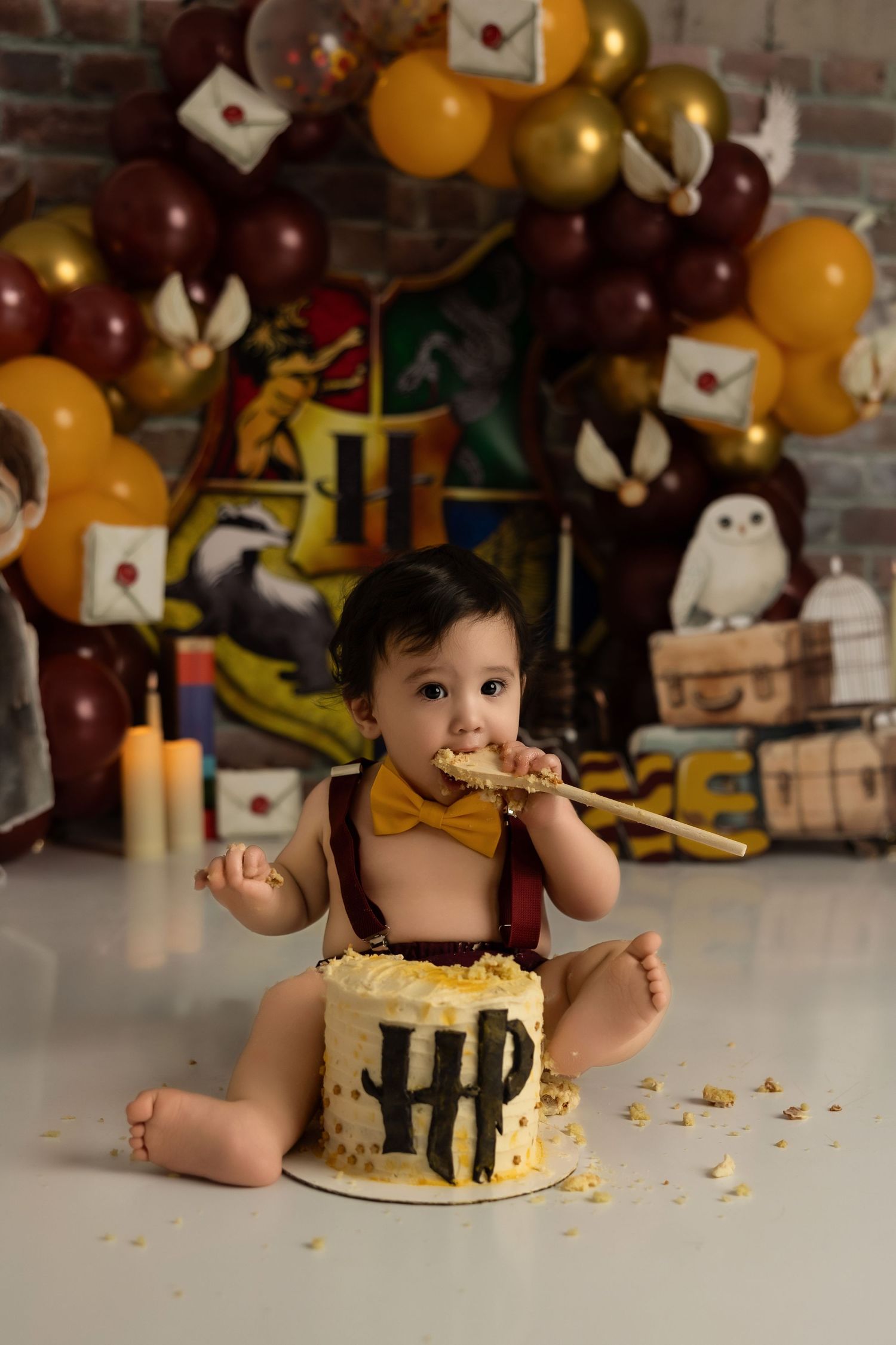 Harry Potter themed birthday cake smash setup with burgundy and gold balloons, floating letters, and magical decorations.