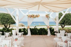 White wedding ceremony setup with flowing fabric canopies overlooking the ocean at a scenic beach location.