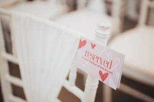 A 'reserved' sign with red heart decorations attached to a white chair at what appears to be a wedding venue.