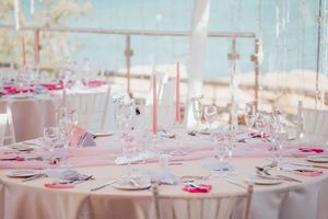 Elegant wedding reception table setup with pink accents, white tablecloths, and crystal glassware overlooking the ocean.