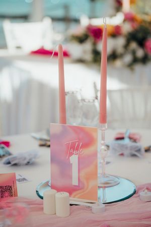 Pink candles and table number display on a wedding reception table with soft pink decor and romantic ambiance.