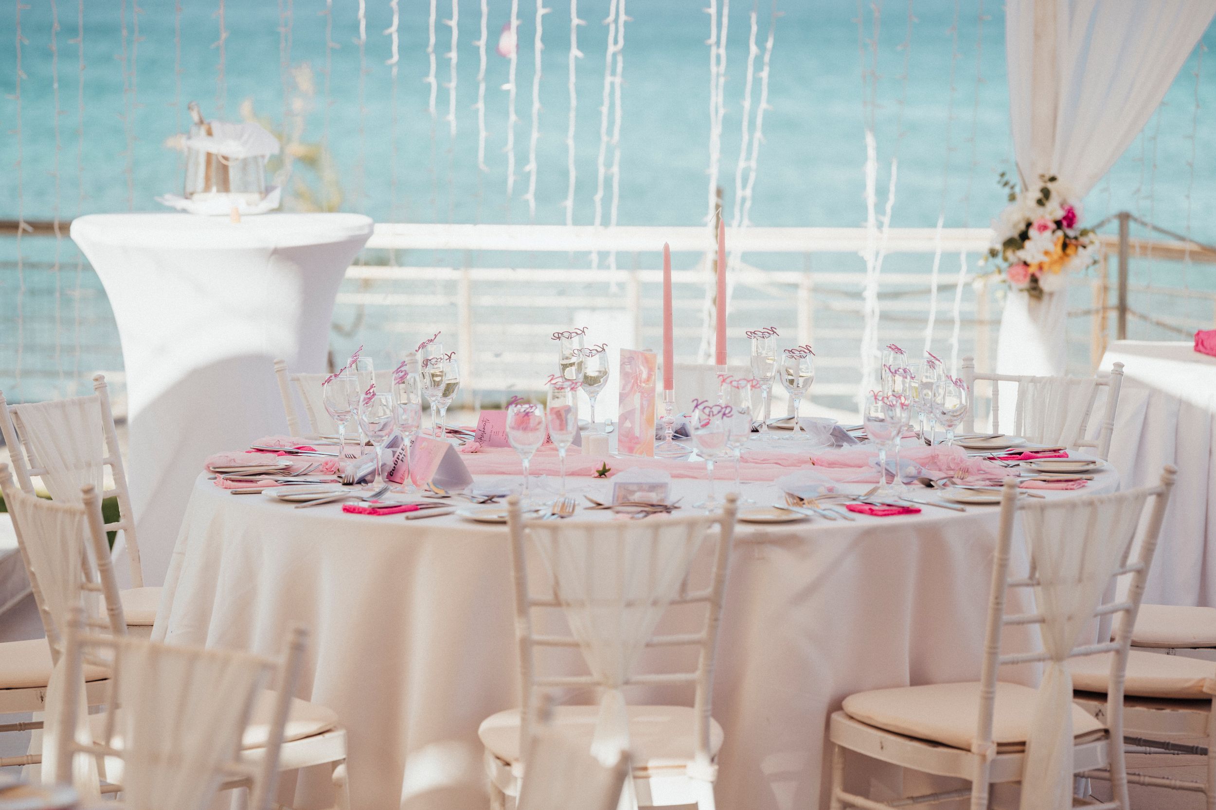An elegant wedding reception venue with round tables decorated in white and pink under draped fabric ceiling.