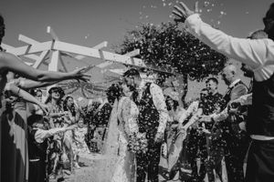 Wedding couple exits ceremony under traditional canopy while guests shower them with celebratory confetti in black and white.