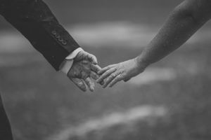 Black and white close-up of two hands reaching out to touch each other against a blurred background.