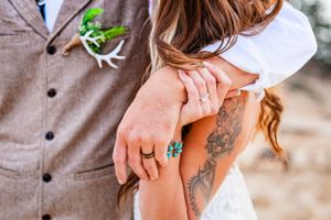 Close up detail of an arm with a tattoo and turquoise ring against formal wedding attire.