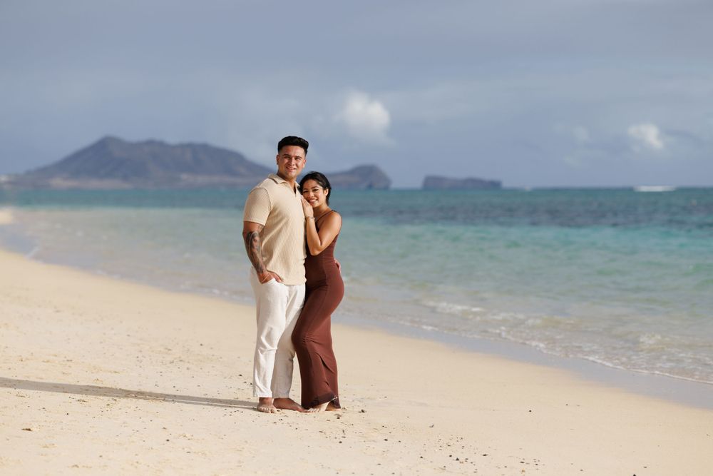 Couple posing together on a white sand beach with turquoise ocean water and island views in the background.