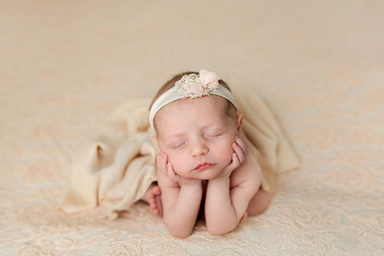 New parents wearing cream-colored clothing gaze lovingly at their newborn baby wrapped in white blanket.