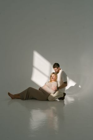 Minimalist maternity portrait with natural window light casting shadows on grey backdrop.