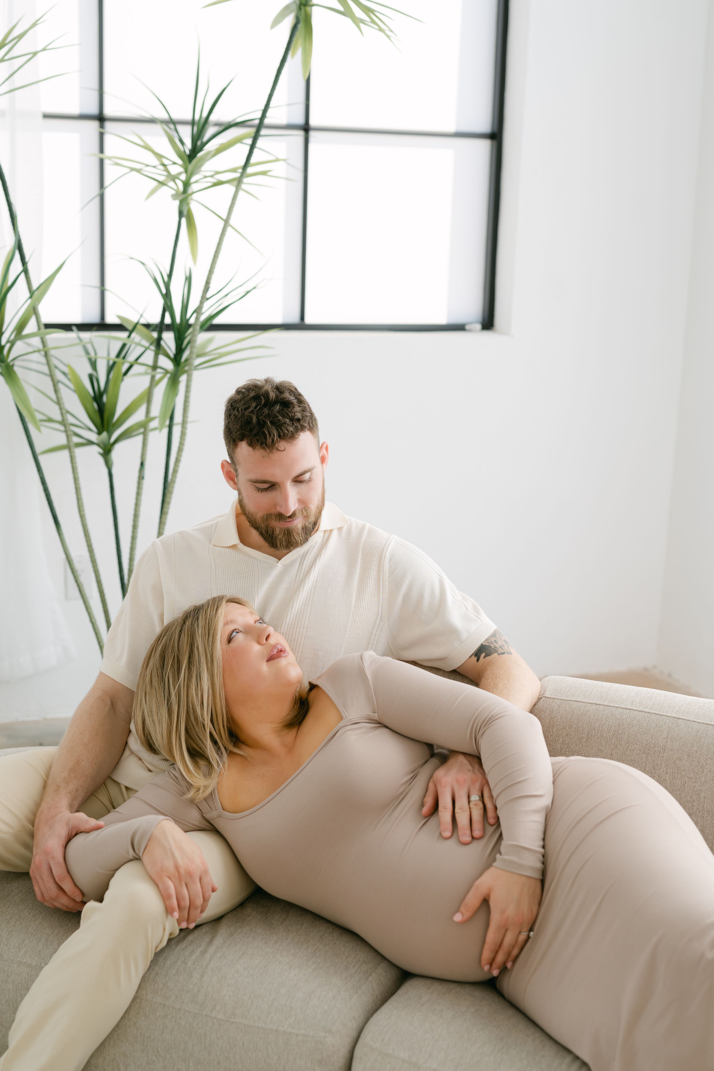 Intimate maternity session capturing relaxed moments on a grey couch in natural light.