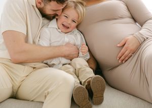 Casual family maternity photos captured on comfortable beige sofa in natural light.