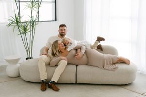 Modern maternity photography in bright white room with indoor plants and minimalist decor.