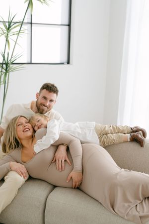 Candid family maternity session showing joyful moments on light grey couch.