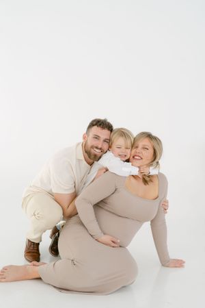 Playful family maternity portraits on white background showing natural interactions.