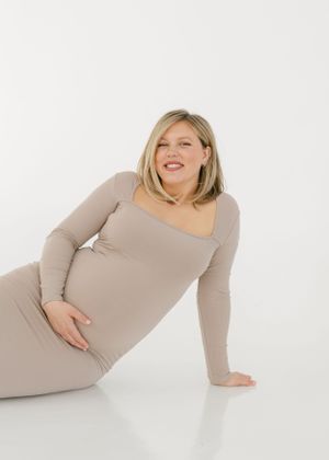 Artistic maternity photos showing a woman in beige dress posing gracefully against white backdrop.