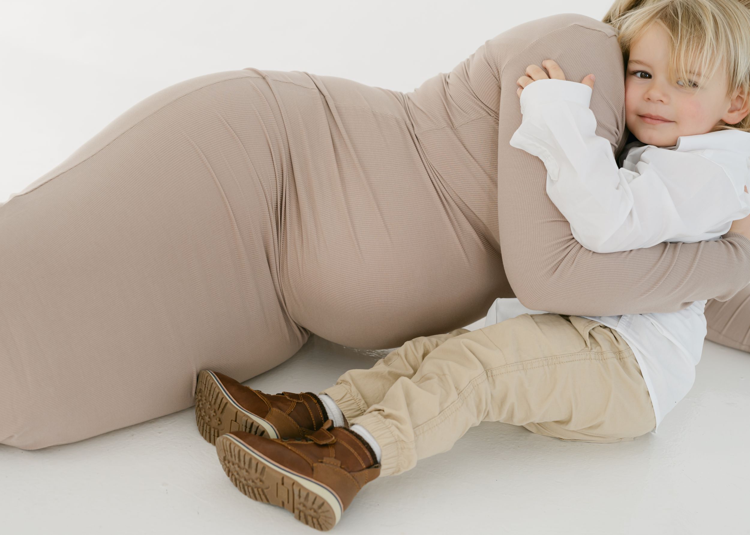 Artistic maternity photos in neutral tones against minimalist white studio backdrop.