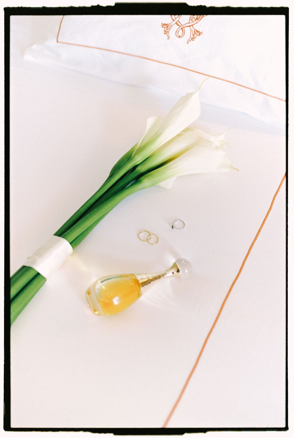 White calla lily stems with wedding rings and gold jewelry against a light background create an elegant wedding detail shot.
