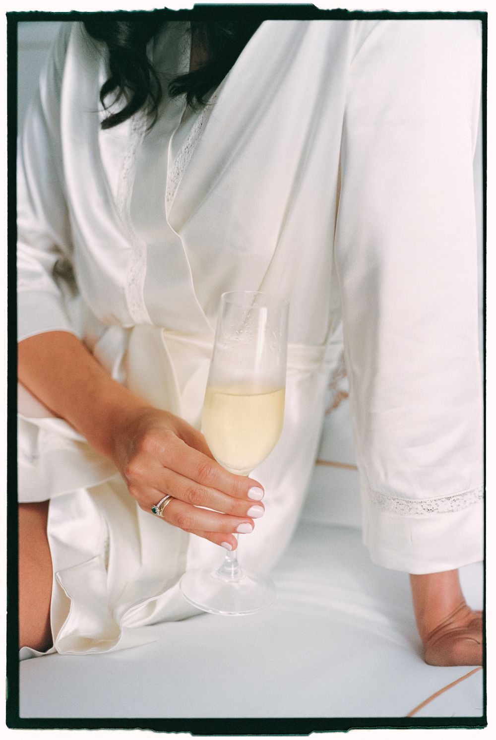 A hand holding a champagne flute while wearing a white robe with lace trim detail.