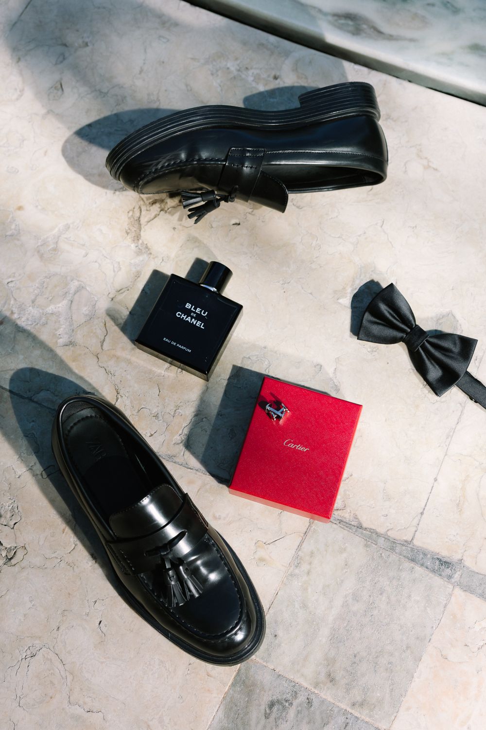 A pair of black leather loafers with classic tassels displayed on a white marble floor.