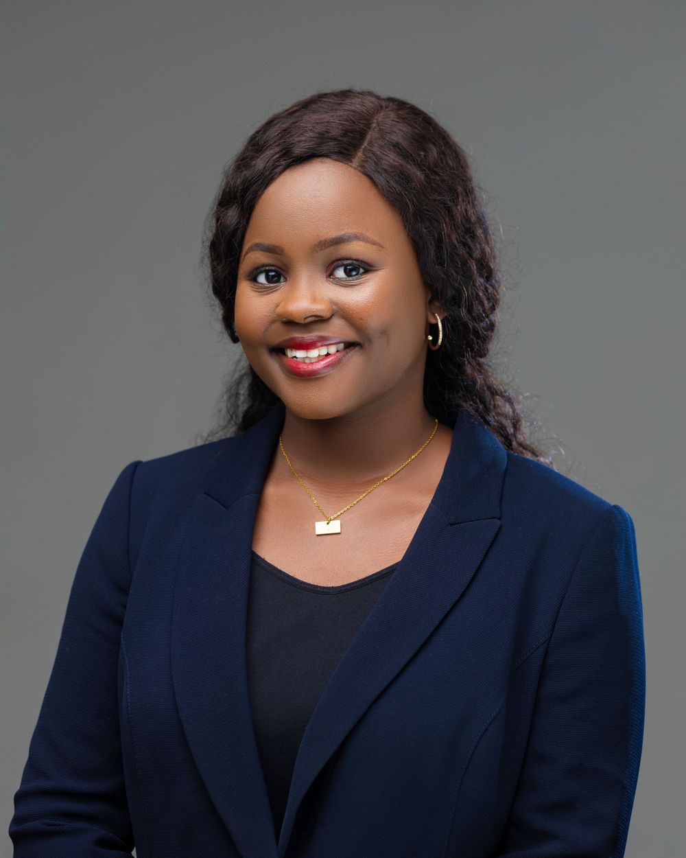Professional headshot of a woman wearing a navy blazer and delicate necklace against gray background.