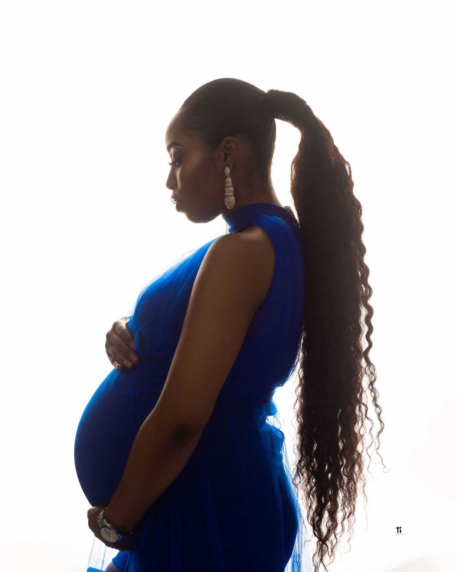 Silhouette of a pregnant woman in a blue dress with long flowing hair against a bright background.