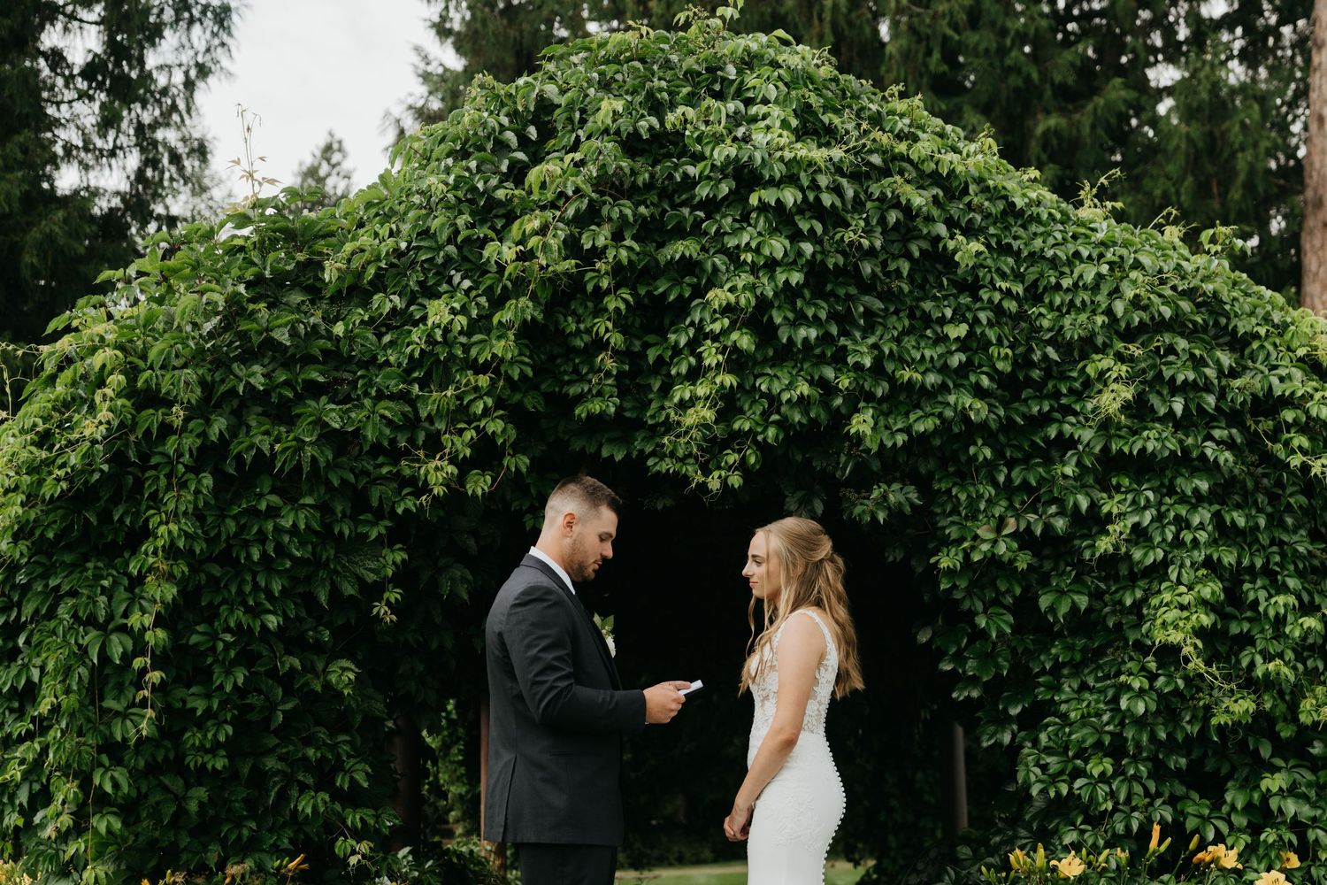 Couple sharing intimate moment under green archway during wedding.